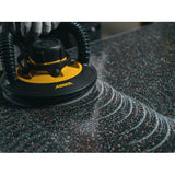 A close-up action shot of a Mirka LEROs sander and Abralon J3 polishing disc, showing the black and yellow tool in motion against a dark speckled countertop with circular sanding patterns visible.