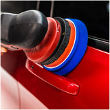 Polishing machine with blue buffing pads on a car surface