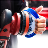 Hand holding a red and black polisher with a blue sanding disc against a blurred background