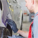 Person working on a car in a garage applying body filler with a spreader