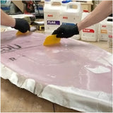 Person applying a MAS Epoxies to fiberglass cloth with gloves and tools in the background.