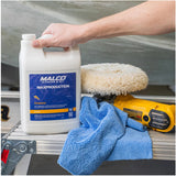 Malco Marine & RV - Presta - MAX Production Compound, 1 Gallon, 165001, image showing person holding bottle in arm in front of a boat, next to a microfiber towel and polisher on a metal bench.