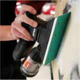 RUPES iBrid HSE73L BLX Mini Sander, 2.75 x 7.75 Inch, image showing sander in action, sanding a panel, using green RUPES ProCut film abrasive sheets with 8-hole vacuum pattern