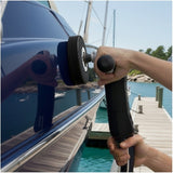 Person applying wax on a boat hull with water and boats in the background